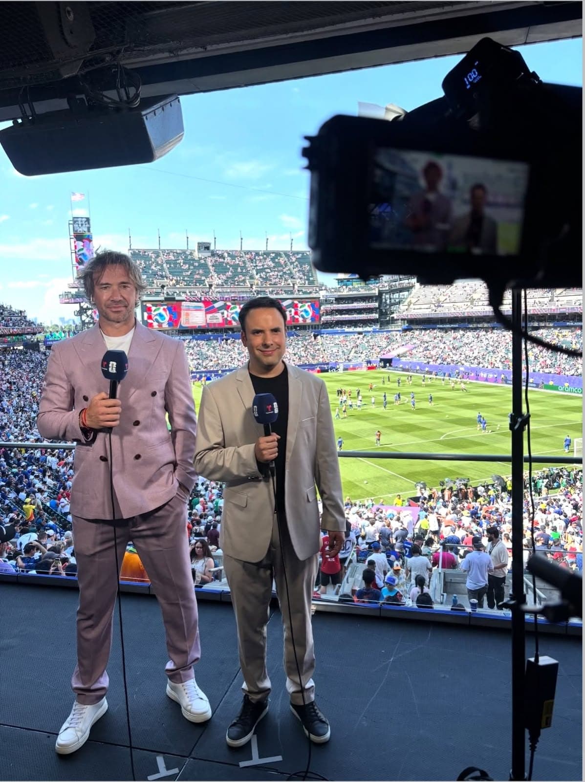 Diego Lugano and a Telemundo journalist in front of the camera, with a packed stadium behind them.